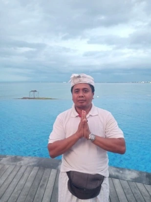 Balinese man in traditional attire praying by infinity pool overlooking ocean.