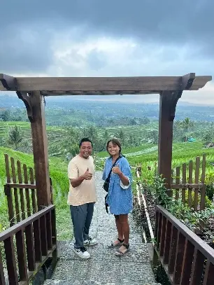 Couple posing under wooden arch overlooking Bali rice terraces.