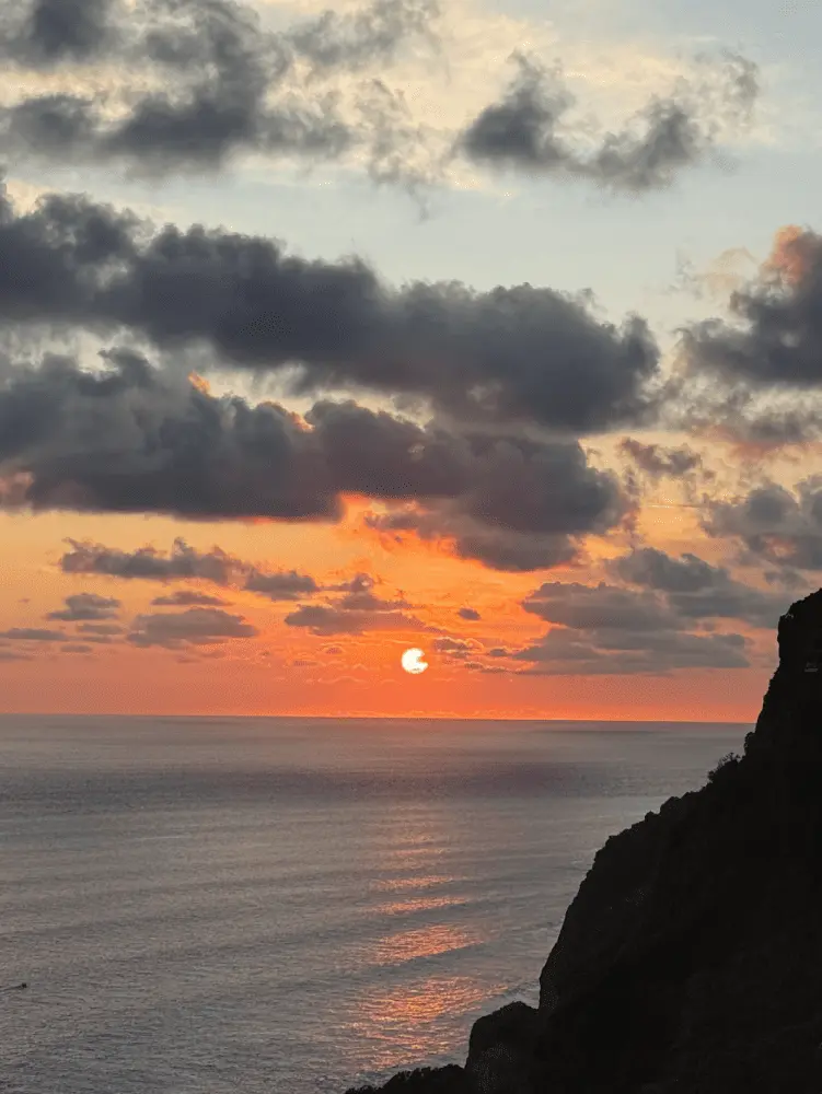 Dramatic sunset over ocean with clouds and cliffside in Bali.
