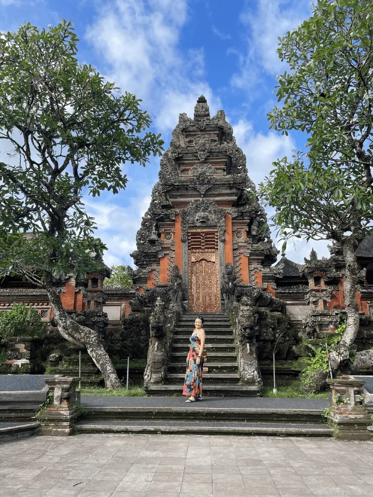 Tourist standing in front of ornate Balinese temple gate during a private Bali day tour with Bali Go Easy, featuring intricate carvings, stone steps, and lush tropical trees under a clear blue sky.
